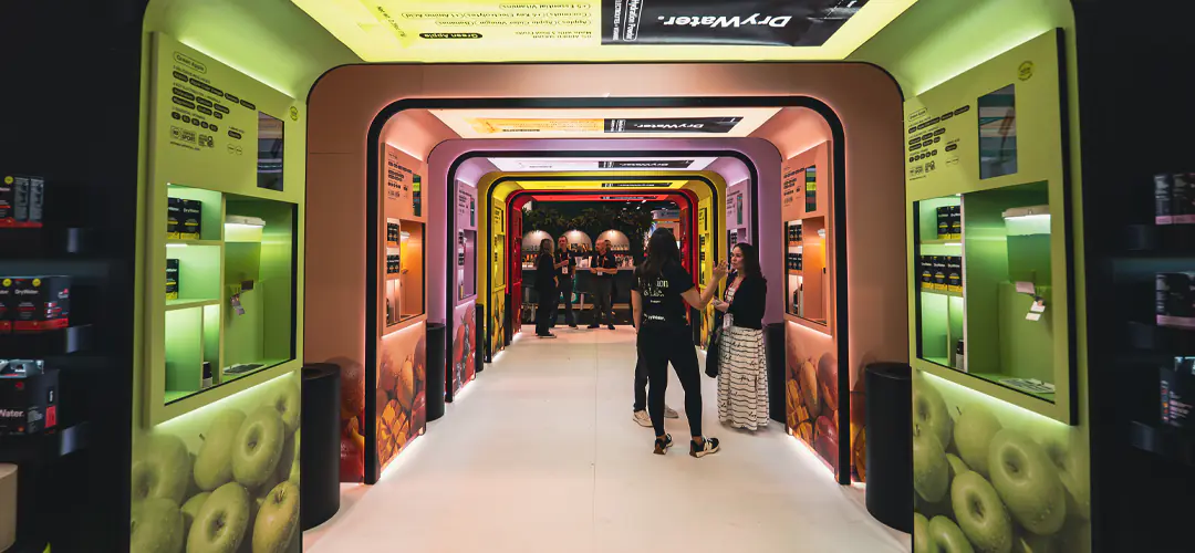 Illuminated experiential trade show booth tunnel with colorful arches and product displays